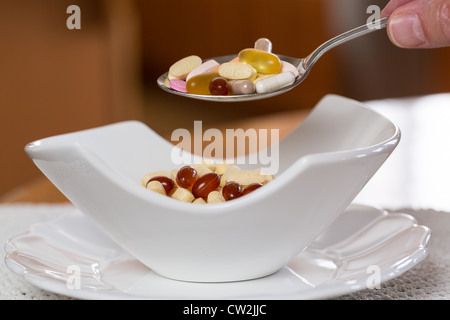 Cucchiaio di compresse di vitamina sospesa sopra il vaso di compresse per la colazione in cucina Foto Stock