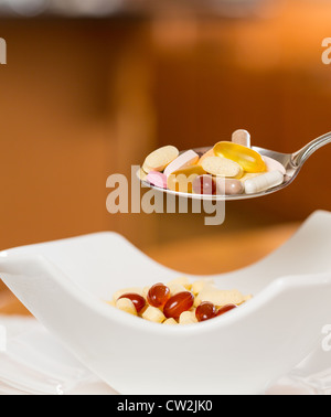 Cucchiaio di compresse di vitamina sospesa sopra il vaso di compresse per la colazione in cucina Foto Stock