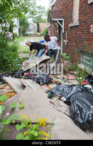 Detroit, Michigan - i membri delle tre miglia di blocco Club tagliare erbe infestanti e rimuovere illegalmente nel cestino di dumping in una casa abbandonata. Foto Stock