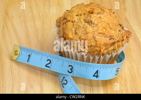 Una carota raisin muffin con un blu nastro di misurazione su un sfondo di legno in una dieta / vivere sano concetto di immagine. Foto Stock