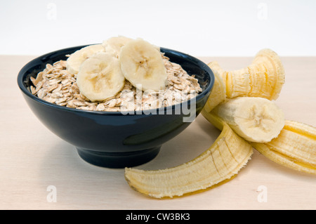 Fiocchi d'avena, o porridge di avena con fette di banana su top nero in ciotola e banana a lato Foto Stock