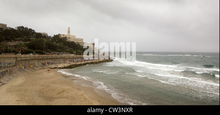 Un seawall con graffiti, spiaggia, Chiesa di San Pietro e il minareto di al-Bahr moschea nella Vecchia Jaffa, Israele Foto Stock