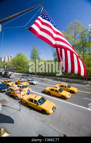 Bandiera americana vola sopra Central Park in primavera con giallo taxi di fronte Helmsely Park Lane, Manhattan, New York City, NY Foto Stock