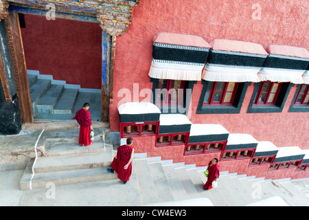 Tre giovani monaci su una scala nella parte anteriore delle pareti rosse al monastero di Thiksey vicino a Leh in Ladakh, India Foto Stock