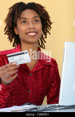 Giovane donna seduta davanti a un computer portatile in possesso di una carta di credito Foto Stock