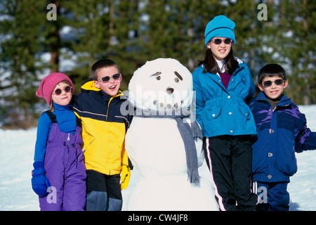 Ritratto di due ragazzi e due ragazze in piedi accanto a un pupazzo di neve Foto Stock