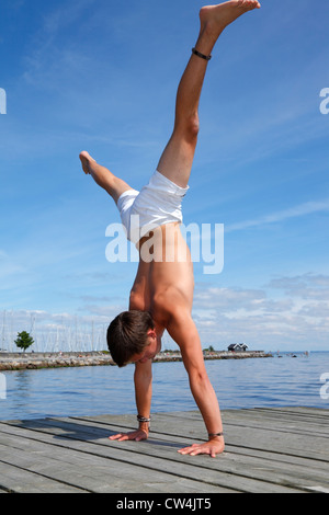 Adolescente di sesso maschile facendo un acrobatico handstand su un pontile sulla spiaggia una calda estate tardo pomeriggio. Foto Stock