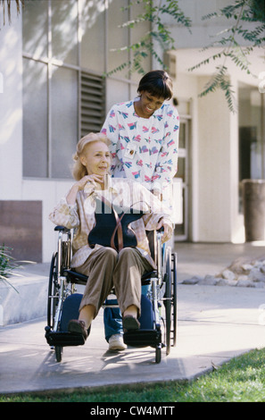 Infermiera femmina spingendo una femmina di un paziente su una sedia a rotelle Foto Stock