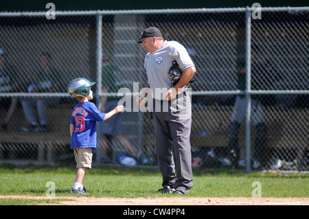 Un cattivo ragazzo fornisce un capoarbitro con un baseball tra gli inning durante una scuola di gioco di baseball. Illinois, Stati Uniti d'America. Foto Stock