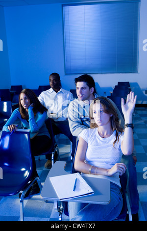 Studenti universitari che frequentano lezioni mentre uno studente con le mani sollevate in aula Foto Stock