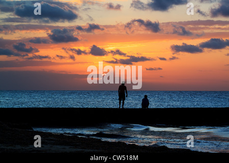 Una giovane coppia guardare il sole andare giù al di sopra del Mare dei Caraibi dal molo sulla costa occidentale dell isola di Cozumel, Messico. Foto Stock