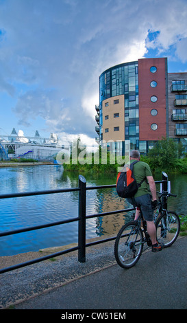 Ciclista maschio lungo il fiume Lea la navigazione mostra il 2012 Stadio Olimpico di Stratford attraverso il canal, Hackney Wick. Foto Stock