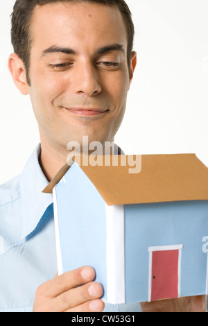Close-up di un giovane uomo che guarda a un modello di una casa e sorridente Foto Stock