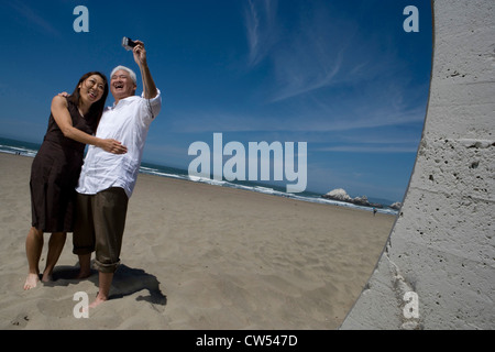 Coppia matura per scattare foto di se stessi e sorridente sulla spiaggia Foto Stock