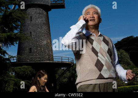 Uomo maturo a parlare su un telefono cellulare con una donna matura in background, Golden Gate Park di San Francisco, California, Stati Uniti d'America Foto Stock
