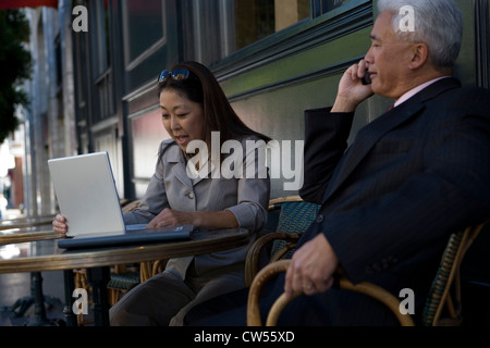 Imprenditrice utilizzando un computer portatile con un imprenditore a parlare su un telefono mobile Foto Stock