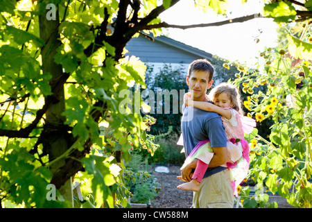Padre dando figlia piggy back ride in giardino Foto Stock
