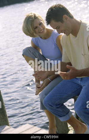 Coppia giovane seduto da un lago di parlare Foto Stock
