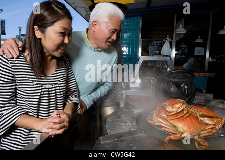 Coppia matura guardando i granchi essendo cotti in un ristorante e sorridente, Fisherman's Wharf di San Francisco, California, Stati Uniti d'America Foto Stock