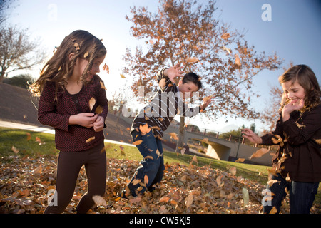 Bambini che giocano su un mucchio di foglie secche in un parco Foto Stock
