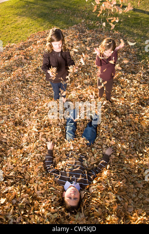 Bambini che giocano su un mucchio di foglie secche in un parco Foto Stock