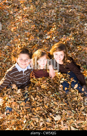 Bambini che giocano su un mucchio di foglie secche in un parco Foto Stock