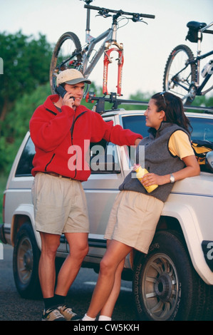 Uomo che parla su un telefono cellulare accanto a una donna appoggiata su una jeep con bici montato alla sommità Foto Stock