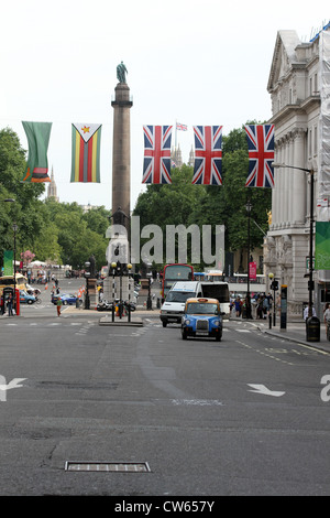 London Red double decker bus e taxi a Waterloo Place London, con Union Jack e altre bandiere sopra Foto Stock