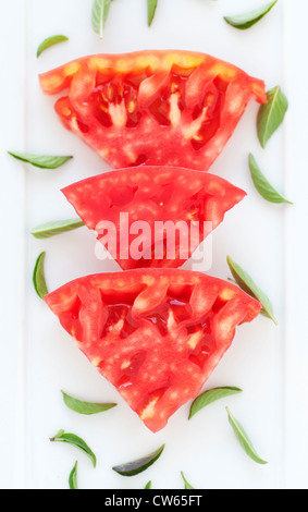 Fette di pomodoro rosso sulla piastra bianca con basilico fresco Foto Stock