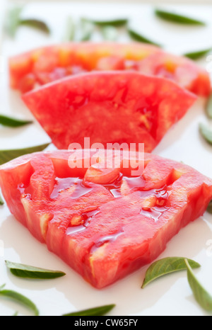 Fette di pomodoro rosso sulla piastra bianca con basilico fresco Foto Stock