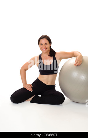Ritratto di una bella e fisicamente la donna nel suo 40s indossare abbigliamento allenamento, sorridente e appoggiate su una palla ginnica. Foto Stock