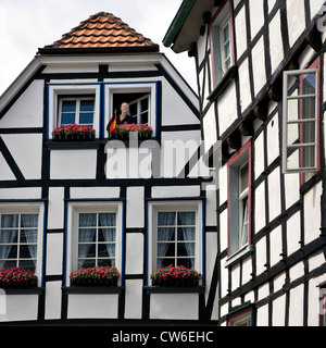 Giovane donna che guarda fuori da una finestra della casa con travi di legno nella storica città vecchia di Hattingen, in Germania, in Renania settentrionale-Vestfalia, la zona della Ruhr, Hattingen Foto Stock