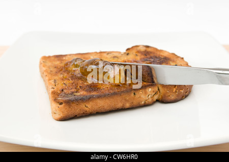 Diffusione di marmellata di arance sulla fetta di pane granaio sulla piastra bianca contro lo sfondo bianco Foto Stock