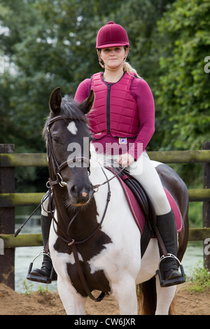 Una giovane donna seduta su un cavallo in una formazione di sabbia anello esterno su una soleggiata giornata estiva Foto Stock