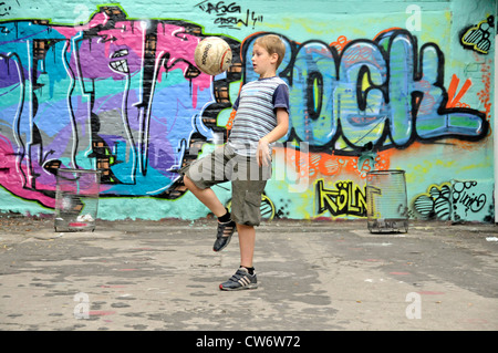 9 anni vecchio ragazzo giocando a calcio davanti ad un muro di graffiti, in Germania, in Renania settentrionale-Vestfalia, Colonia Foto Stock