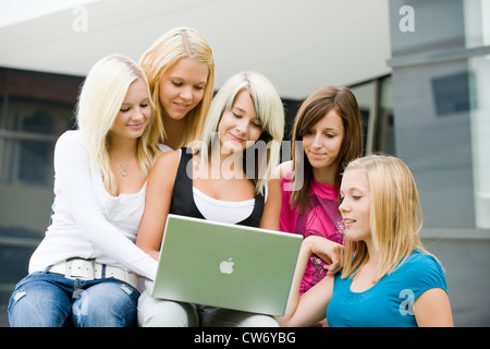 Cinque ragazze giovani riuniti attorno a un computer portatile guardando lo schermo con un sorriso Foto Stock