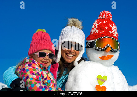 Madre e figlia in vacanza invernale con pupazzo di neve, Francia Foto Stock