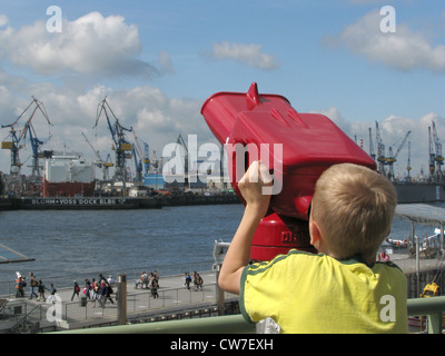 Giovane ragazzo sta guardando attraverso un binocolo su per le banchine al Landungsbruecken nel porto di Amburgo, Germania, Amburgo Foto Stock