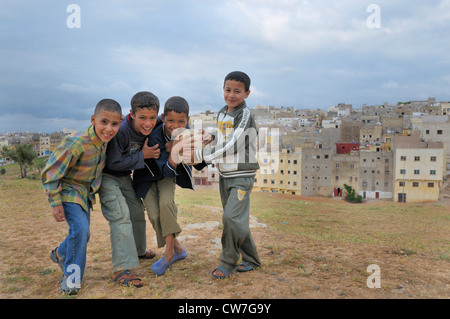 Roguish ragazzi con il calcio guardando nella telecamera, povero quater in background, Marocco, Fes Foto Stock