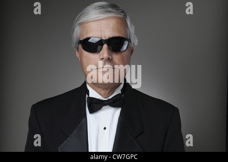Ritratto di un grave alla ricerca di uomo di mezza età in uno smoking e occhiali da sole. Formato orizzontale su uno sfondo grigio. Foto Stock
