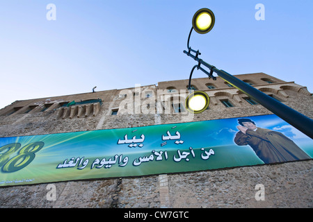 Banner di propaganda raffigurante capo di stato Gheddafi sulla facciata del vecchio castello Spagnolo Saraya al-hamra dal XVI secolo al quadrato verde al tramonto, Libia, Tripolis Foto Stock