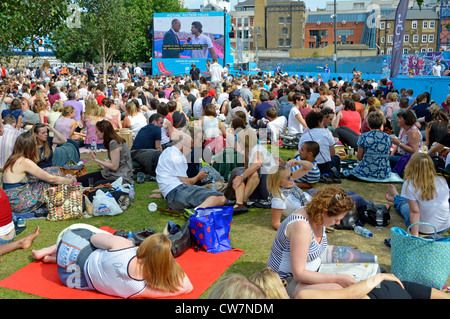 La folla di persone si siede sull'erba guardando le Olimpiadi di Londra del 2012 TV sport evento grande schermo televisivo esterno in Potters Fields Park Southwark Inghilterra Regno Unito Foto Stock