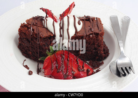 Un piatto di brownie al cioccolato con panna e fragole. Foto Stock