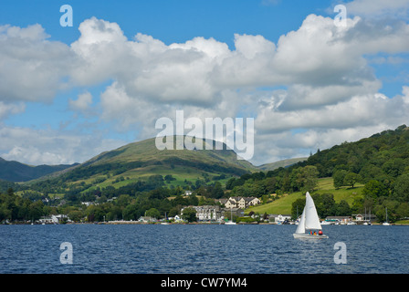 Barca a vela sul lago di Windermere, con Waterhead - e rosso ghiaioni - in background, Parco Nazionale del Distretto dei Laghi, Cumbria Regno Unito Foto Stock