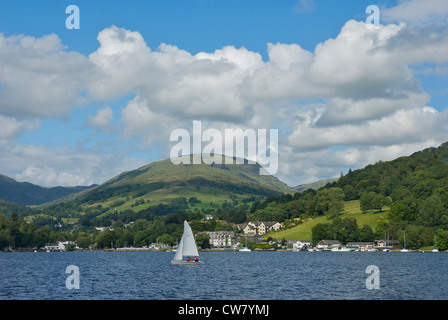 Barca a vela sul lago di Windermere, con Waterhead - e rosso ghiaioni - in background Foto Stock