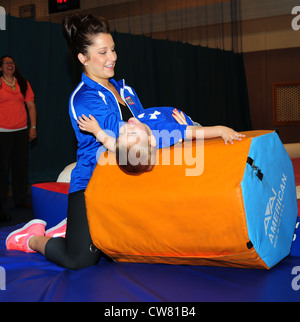 Carly Patterson, ginnasta olimpionica e medaglia d'oro, aiuta Christian graham, 2, pratica un rotolo indietro durante una toddlersâ€™ di classe di ginnastica aug. 13, 2012, presso la raf mildenhall centro giovanile. Patterson era 16 quando ha vinto la sua medaglia d'oro ad Atene, Grecia, nel 2004. ha visitato la base come parte di un regno servizi tour dell'organizzazione. Foto Stock