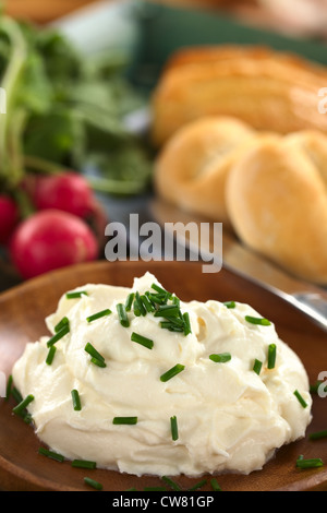 Panna fresca, formaggio fuso sul piatto di legno con erba cipollina sulla parte superiore, il ravanello e panini nel retro Foto Stock