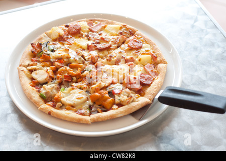 Pizza con le salsicce, prosciutto, pollo, peperone, ananas su una piastra bianca. Foto Stock