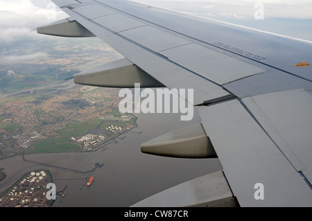 Aereo commerciale (Airbus A319) volando sopra la Coryton Thames Haven olio facilitiy storage, Essex, Regno Unito. Foto Stock