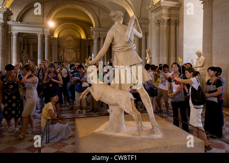 Ai turisti di ammirare la statua di Diana di Versailles, leggermente su lifesize statua in marmo della dea greca Artemide (latino: Diana), con un cervo, situato nel Musée du Louvre di Parigi. Si tratta di una copia romana (1 ° o 2 ° secolo D.C.) di perdita del greco originale di bronzo attribuito a Leochares, c. 325 BC. La statua è anche noto come Diana à la Biche, Diane Chasseresse (Diana cacciatrice'), Artemis di Chase e Artemis con zampe posteriori. Foto Stock